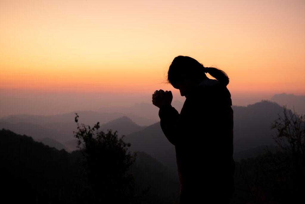 Silhouette of girl praying over beautiful sky background. Christ