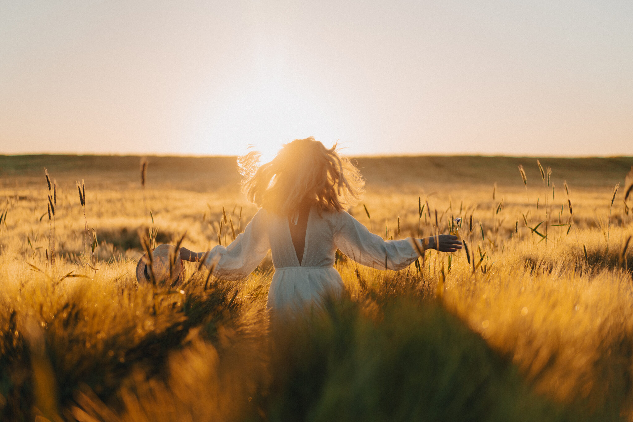 young beautiful woman with long blond hair in a white dress on a wheat field in the early morning at sunrise. Summer is the time for dreamers, flying hair, a woman running across the field in the rays of the sun. travels