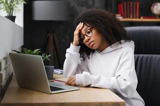 Stressed young adult looking at phone or laptop with hands over face, representing the weight of financial hardship and feeling behind peers while trying to trust God during hard times